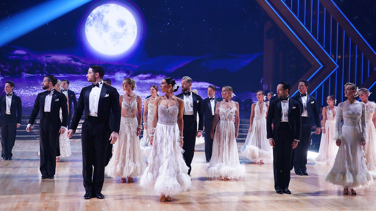 All male dancers in black tuxedos and female dancers in white on the ballroom floor of "Dancing with the Stars"