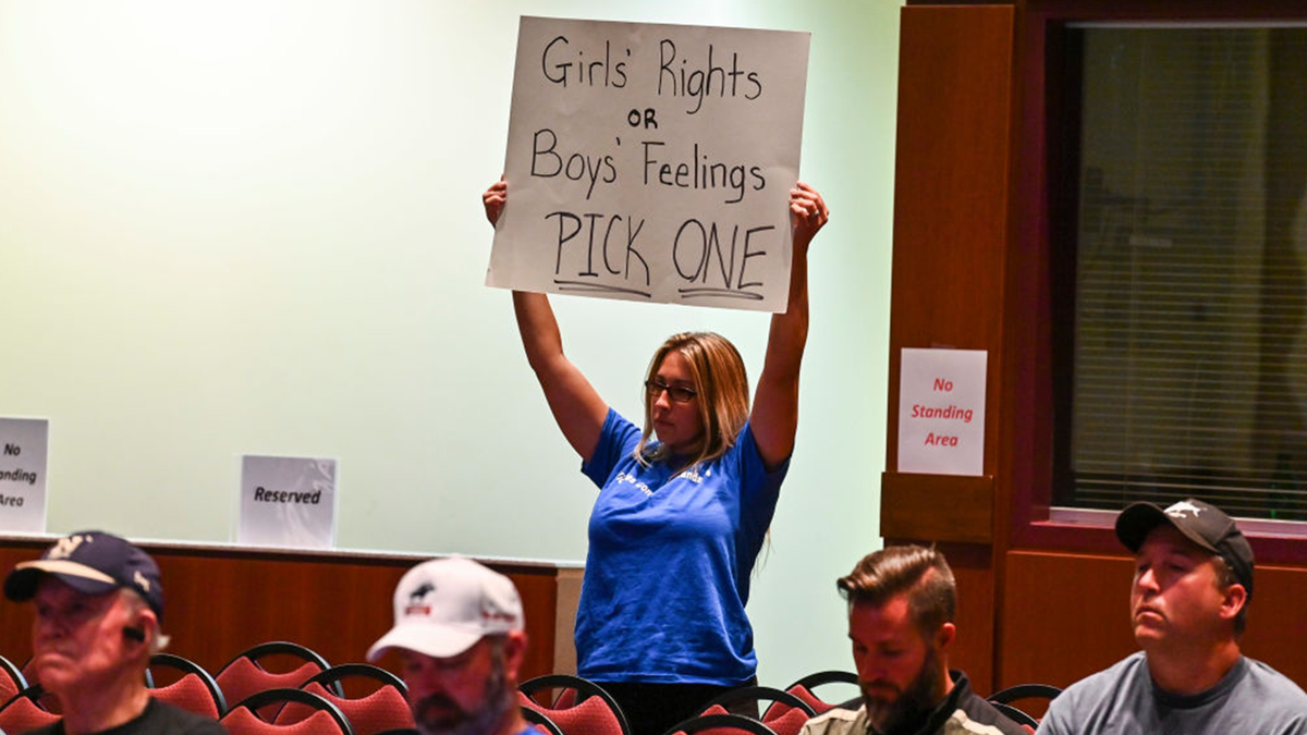 Woman holds a sign at a school board meeting