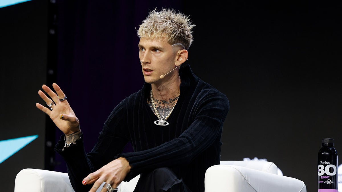 Machine Gun Kelly wears blue sweater and gold chain on stage