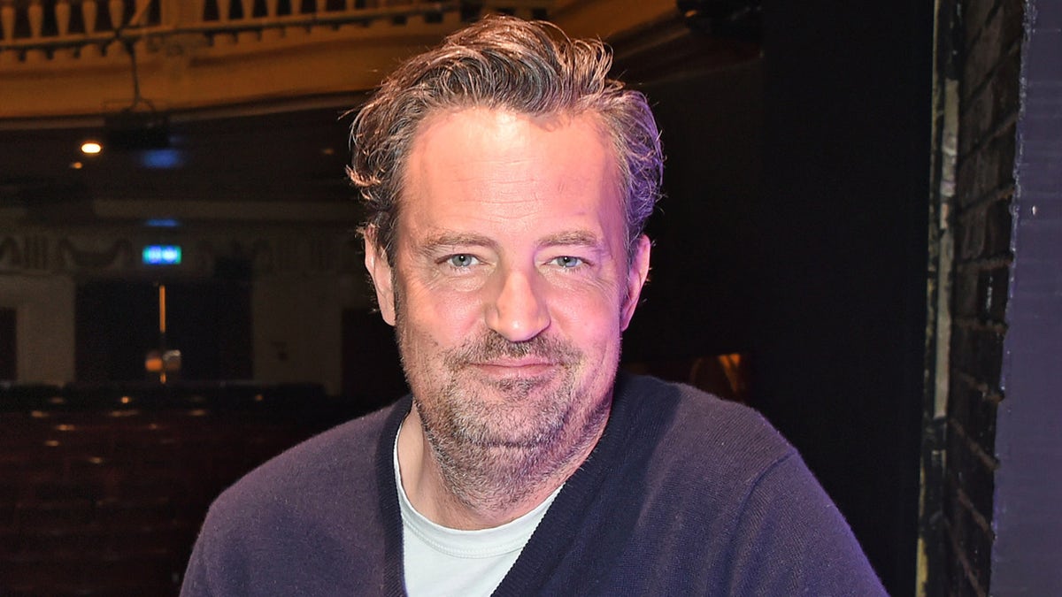 Matthew Perry indossa un maglione blu e una maglietta durante l'evento