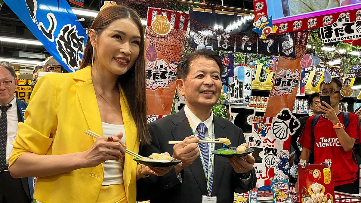 Japanese Agriculture Minister Ichiro Miyashita, right, and Malaysian celebrity Amber Chia hold scallops with chopsticks
