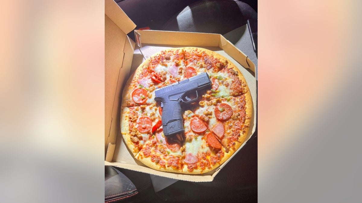 A handgun on top of a pizza inside a pizza box on a car seat