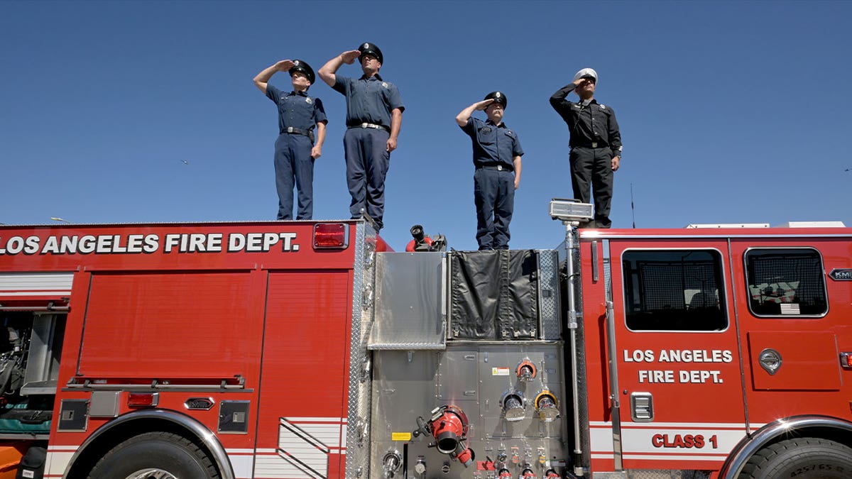 Firefighters stand and salute on a fire truck 