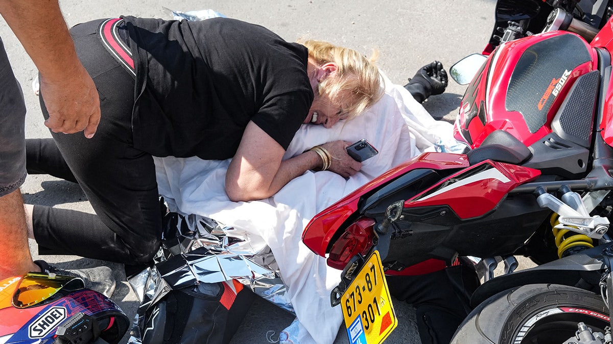 Woman weeps over covered body next to red motorcycle