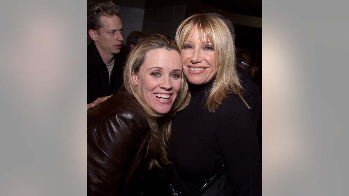 Jenny McCarthy in a leather jacket hugs Suzanne Somers in a brown jacket in a picture from 2002