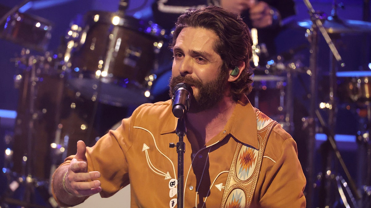 Thomas Rhett wears an orange shirt and sings into the microphone at the CMT Music Awards