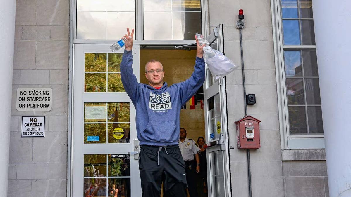 Massachusetts blogger Turtleboy Aiden Kearney raises hands in the arm with "Free Karen Read" hoodie as he leaves courthouse