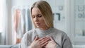 stressed adult female with blonde hair feeling sick at home apartment and touching heart area, cardiac pain symptom