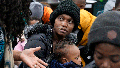 Haitian immigrant Rose Juliane, center, holds her daughter Rosie Sarah, as she speaks with Immigrant Family Services Institute Executive Director Geralde Gabeau, left, while waiting at the agency in the Mattapan neighborhood of Boston for transportation to a shelter on Nov. 16, 2023.