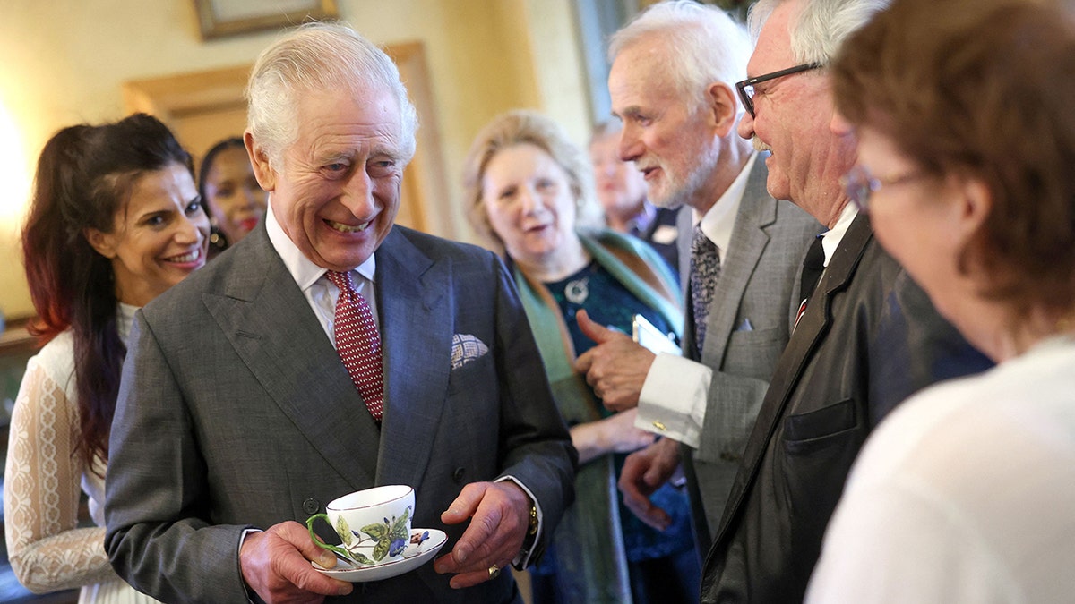 Rei Charles sorrindo enquanto segura uma xícara e um pires