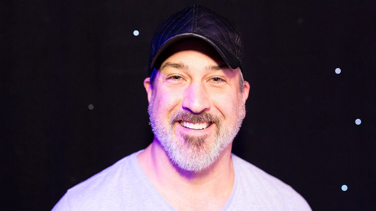 Joey Fatone smiles in a grey t-shirt and black hat 