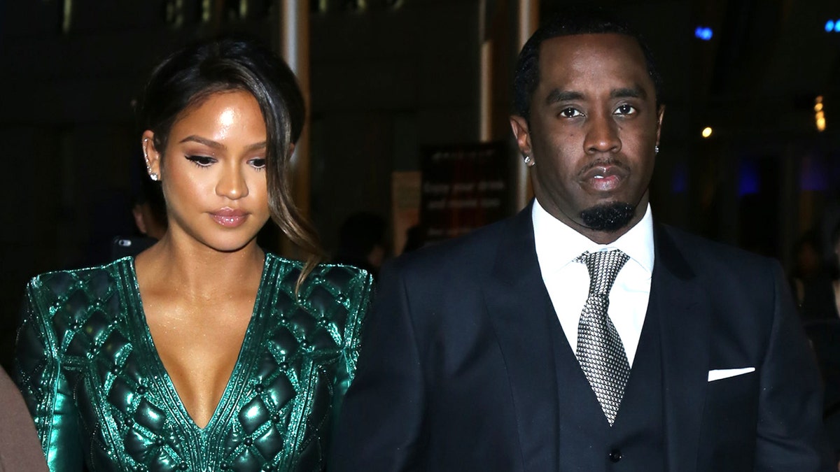 Cassie in an emerland green shiny dress walks with Diddy in a suit