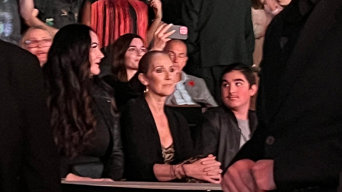Celine Dion em um terno preto sentada assiste Katy Perry se apresentar em Las Vegas