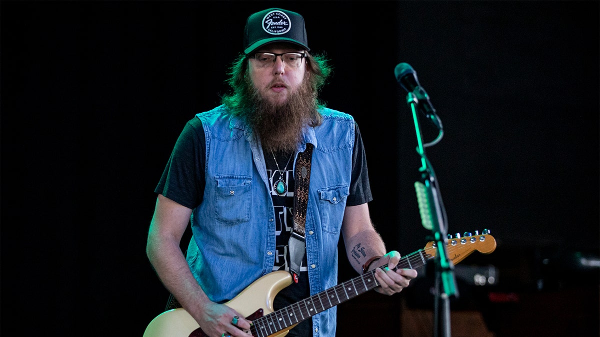 Country musician Cody Tate playing a guitar on stage wearing a baseball cap