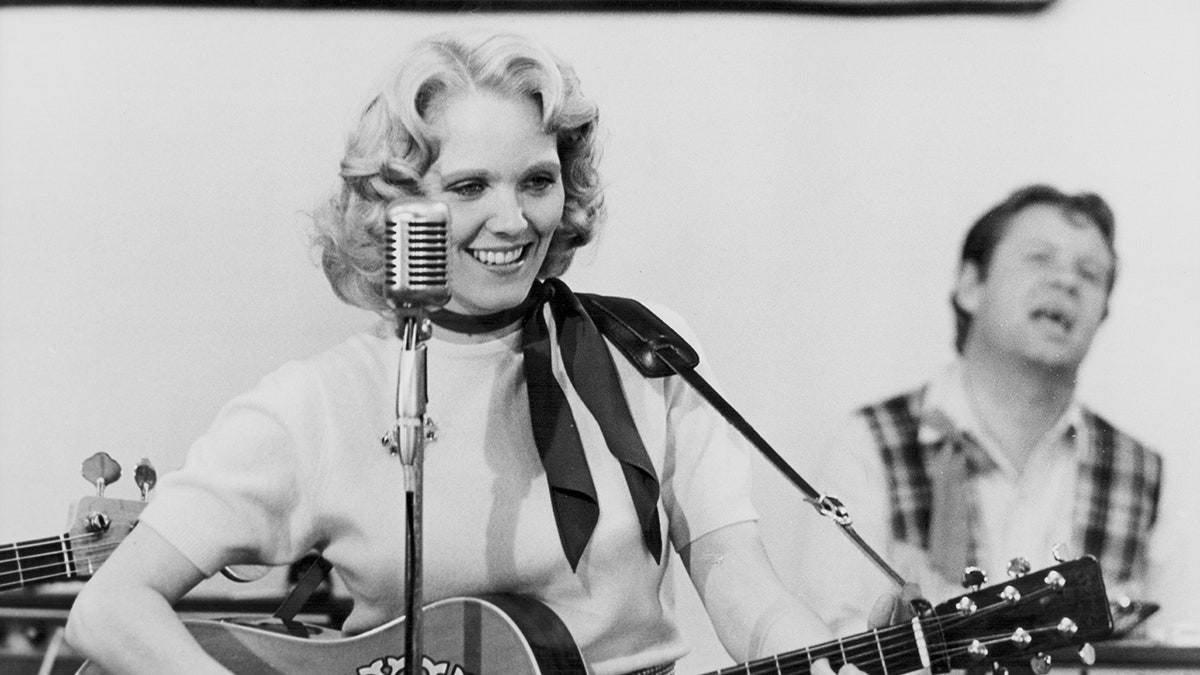 Conny Van Dyke holding a guitar and smiling near a microphone