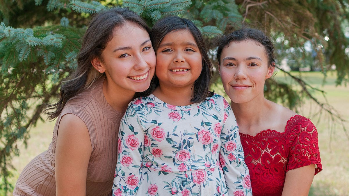 Three girls smiling, girl in midlde is younger