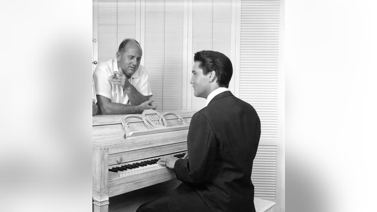 Elvis Presley playing a piano in front of Colonel Tom Parker