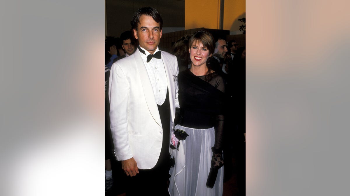 Mark Harmon in a white tuxedo holds hands with his wife in a black top and blue skirt at hte People's Choice Awards