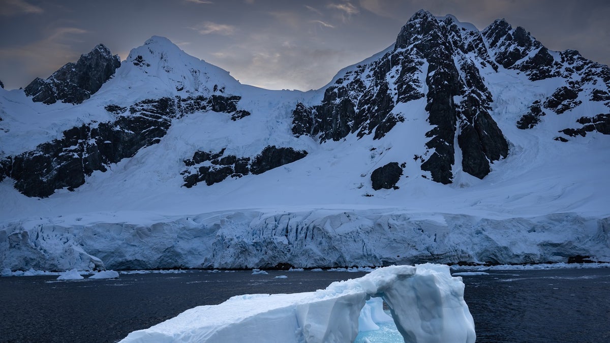 An iceberg near Antarctica, with snow-covered mountains behind it