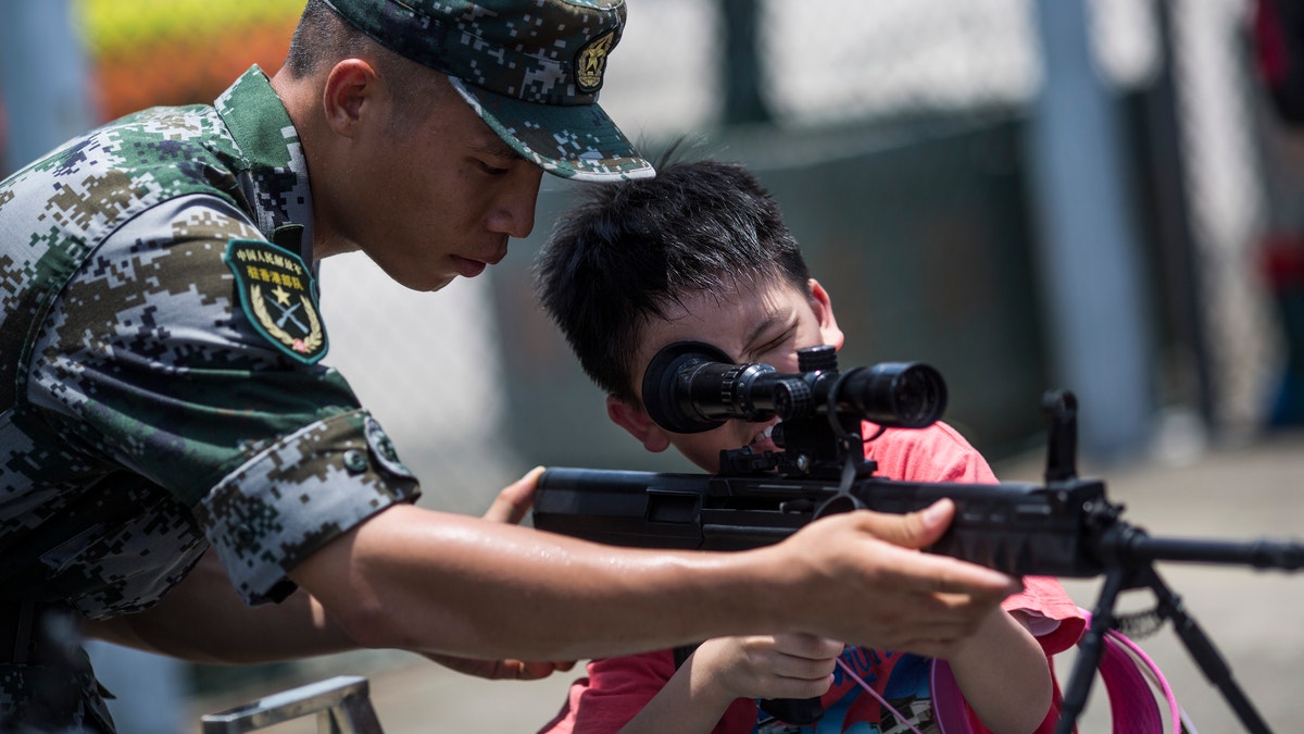 Chinese soldier coaching boy on rifle handling