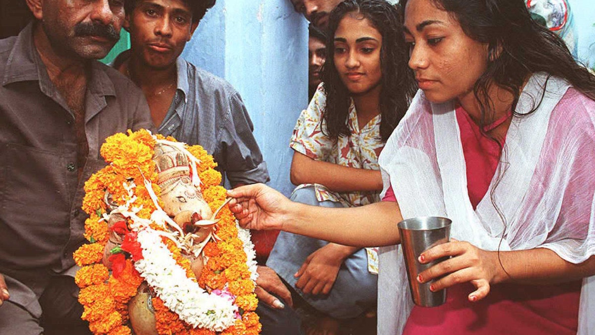 woman feeding milk to a statue of Ganesh