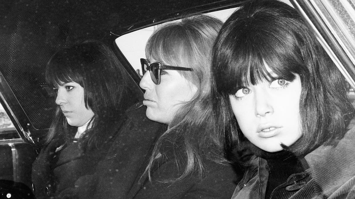 Three Beatles wives looking serious sitting together in a car