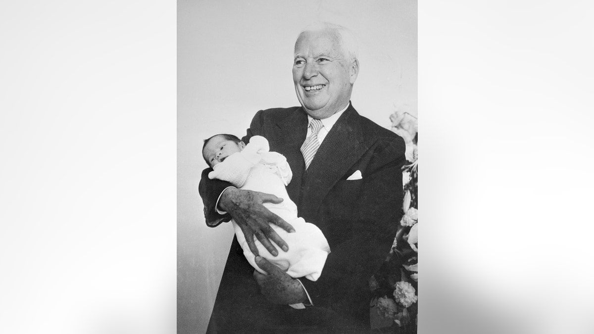 Charlie Chaplin smiling in a suit holding his baby