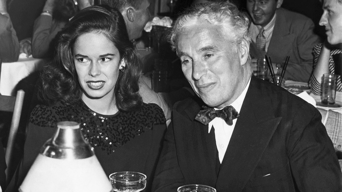 Oona sitting next to her husband Charlie Chaplin wearing a suit and bow tie