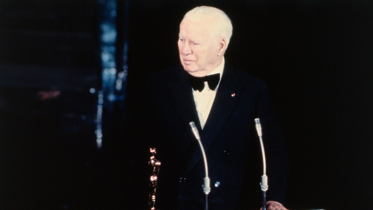 Charlie Chaplin in front of the stage and mic wearing a suit and bow tie