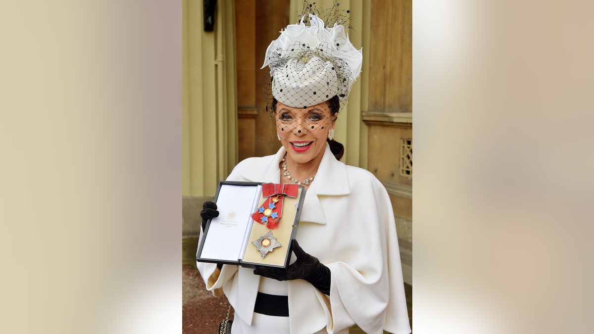 Joan Collins holding her award while wearing a fascinator
