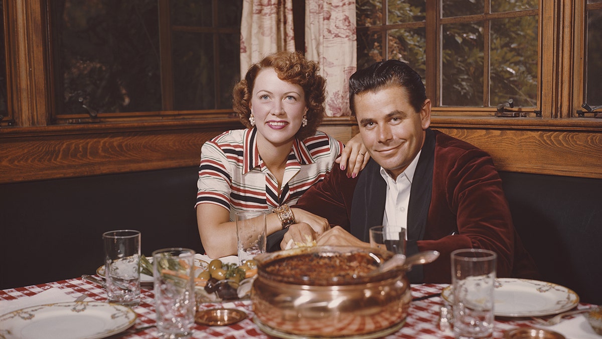 Glenn Ford and Eleanor Powell smiling while sitting at the dinner table