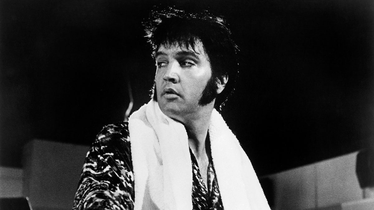 Elvis Presley olhando para longe com uma toalha enrolada no pescoço