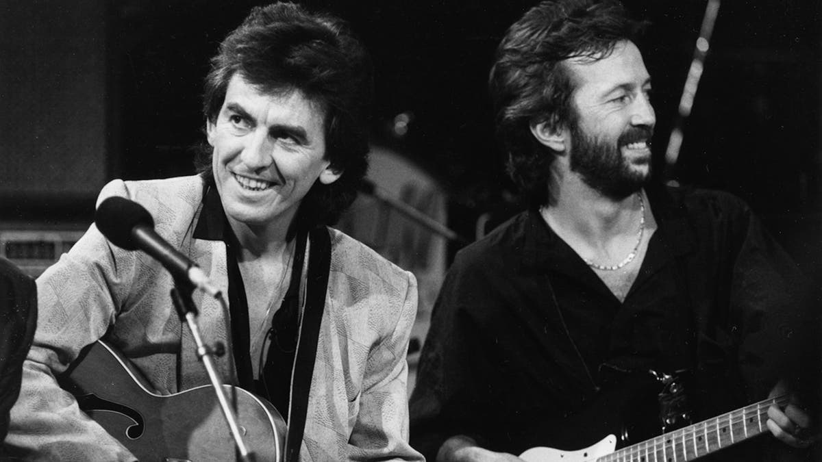 George Harrison and Eric Clapton playing guitar together on stage and smiling