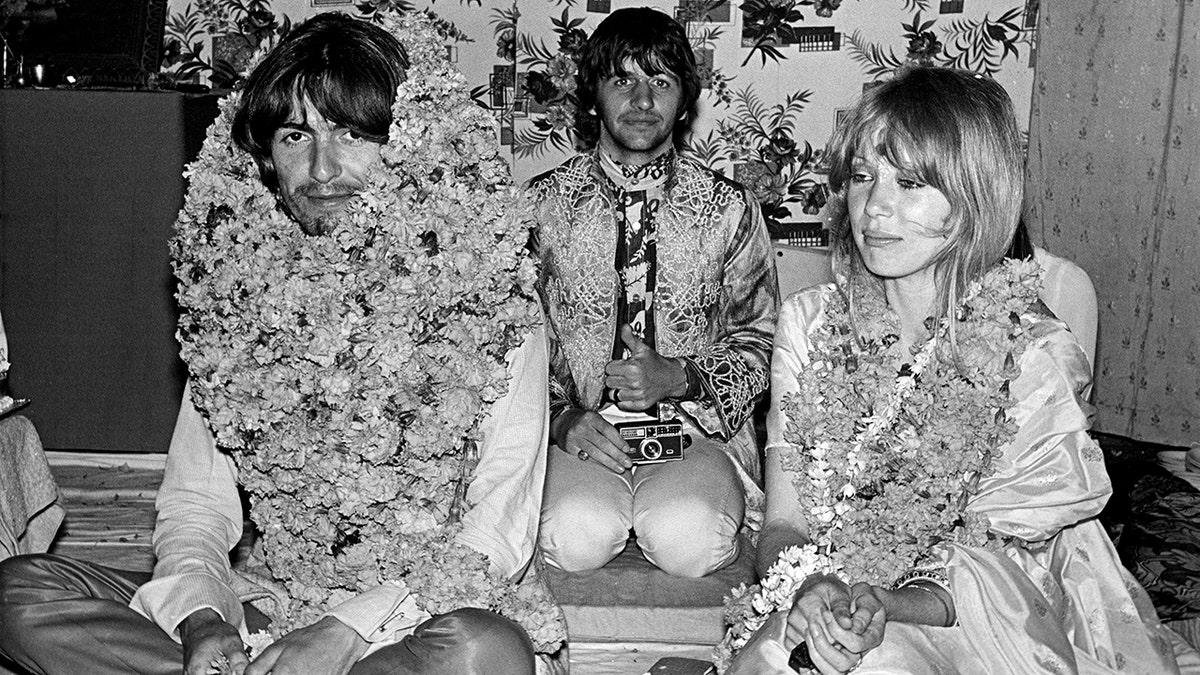 George Harrison, Ringo Starr and Pattie Boyd sitting next to each other covered in flowers