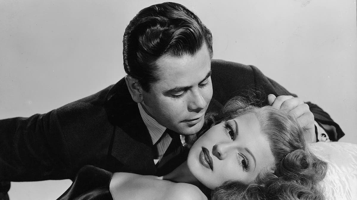 Glenn Ford si china per ricevere un bacio da Rita Hayworth