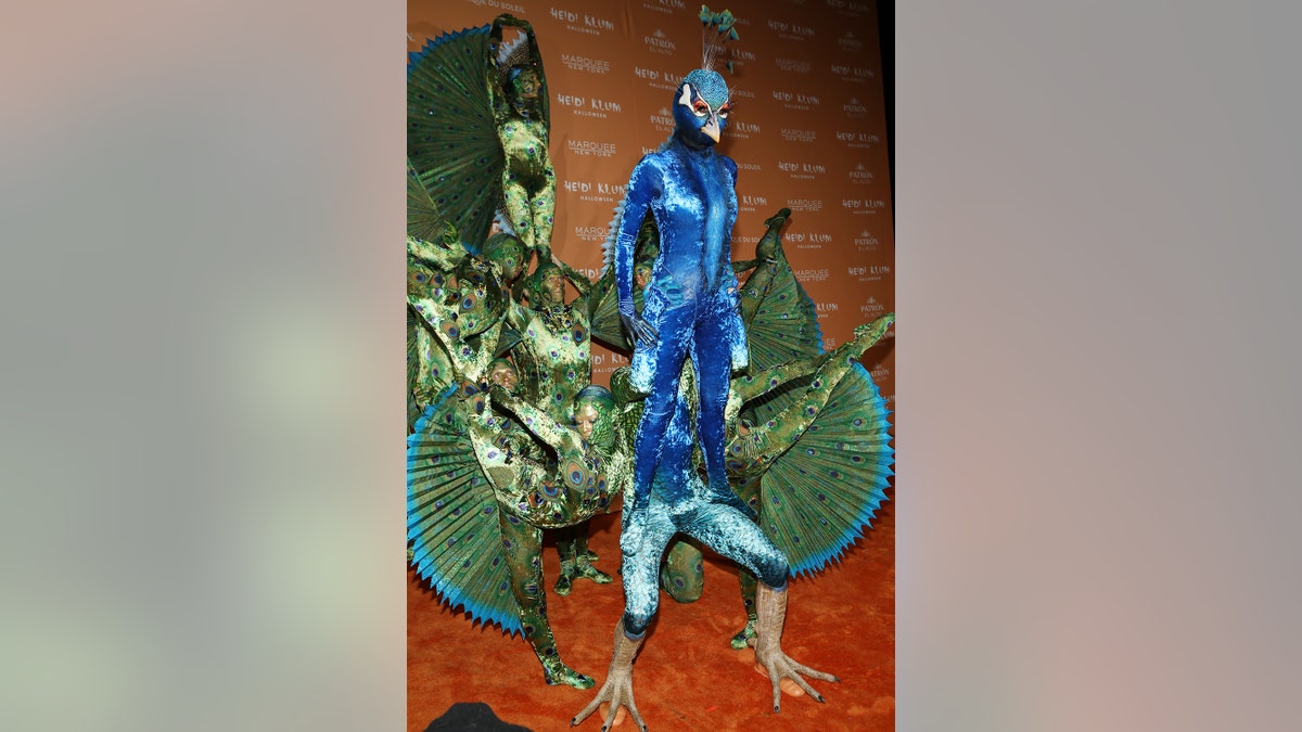 Heidi Klum standing on top of a costumed person dressed up as a peacock