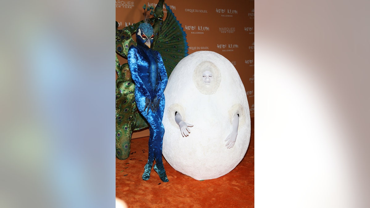 Heidi Klum dressed as a peacock next to her husband dressed up as an egg