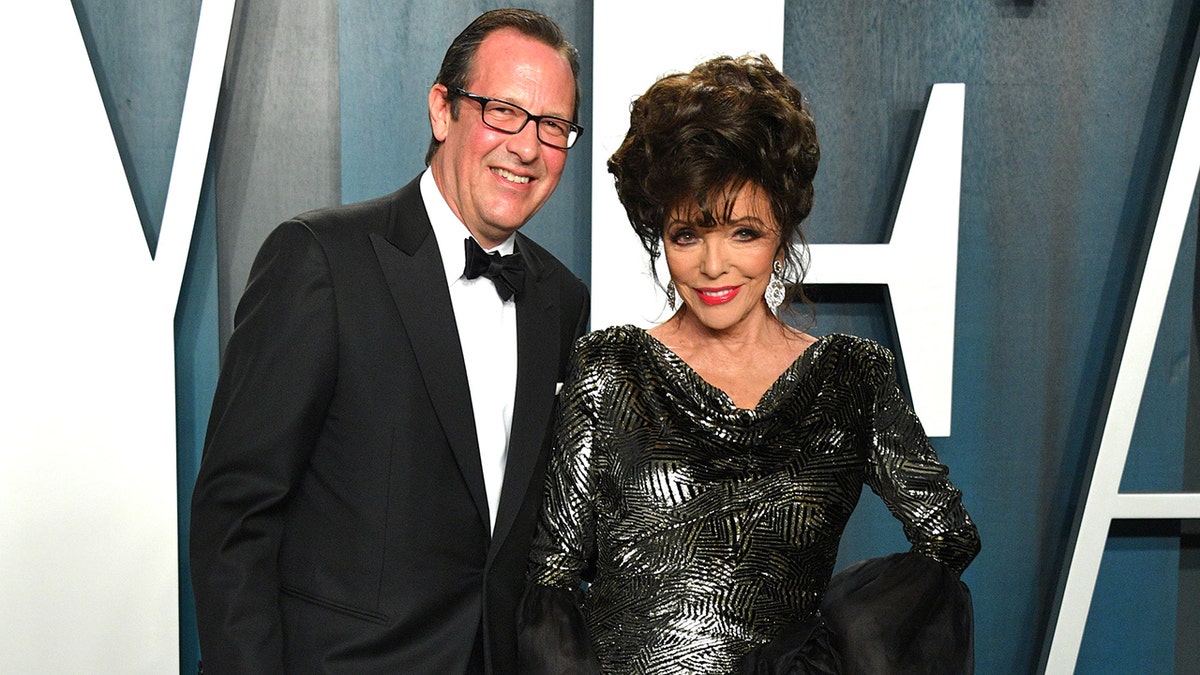 Joan Collins wearing a dark silver gown next to Percy Gibson wearing a tux