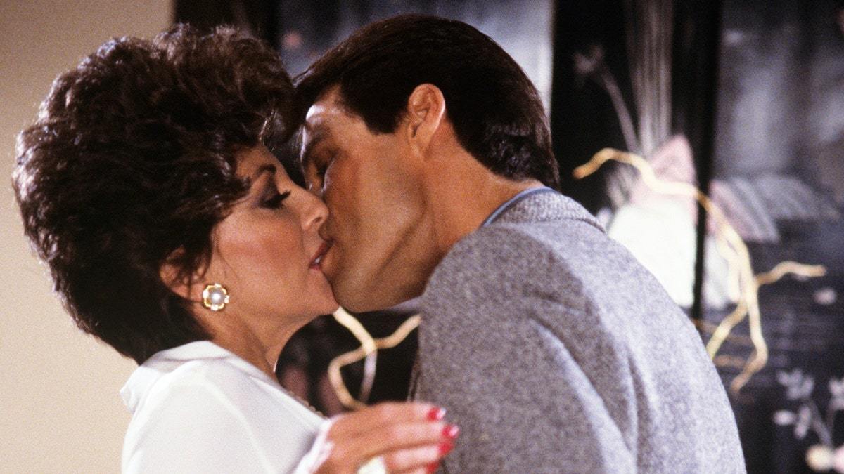 Joan Collins wearing a white dress getting kissed by Michael Nader