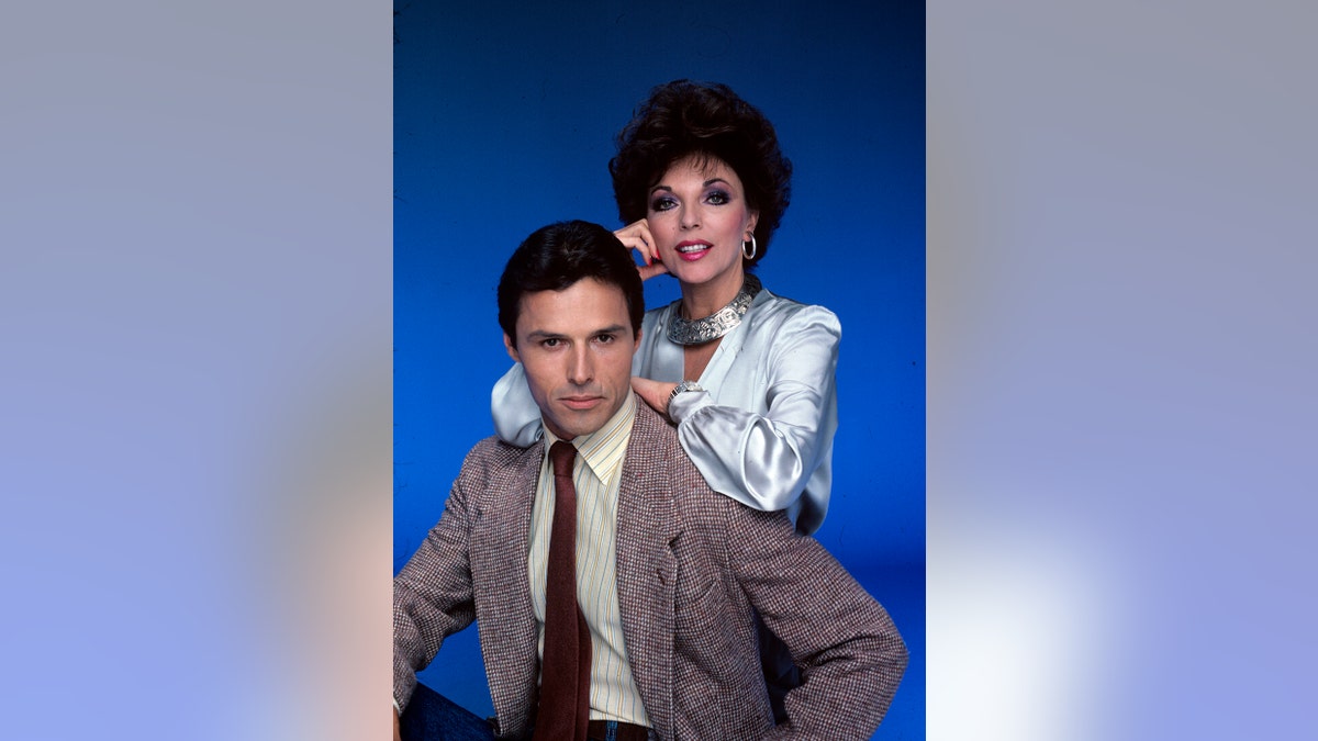 Joan Collins leaning on Michael Nader during a glamorous photoshoot