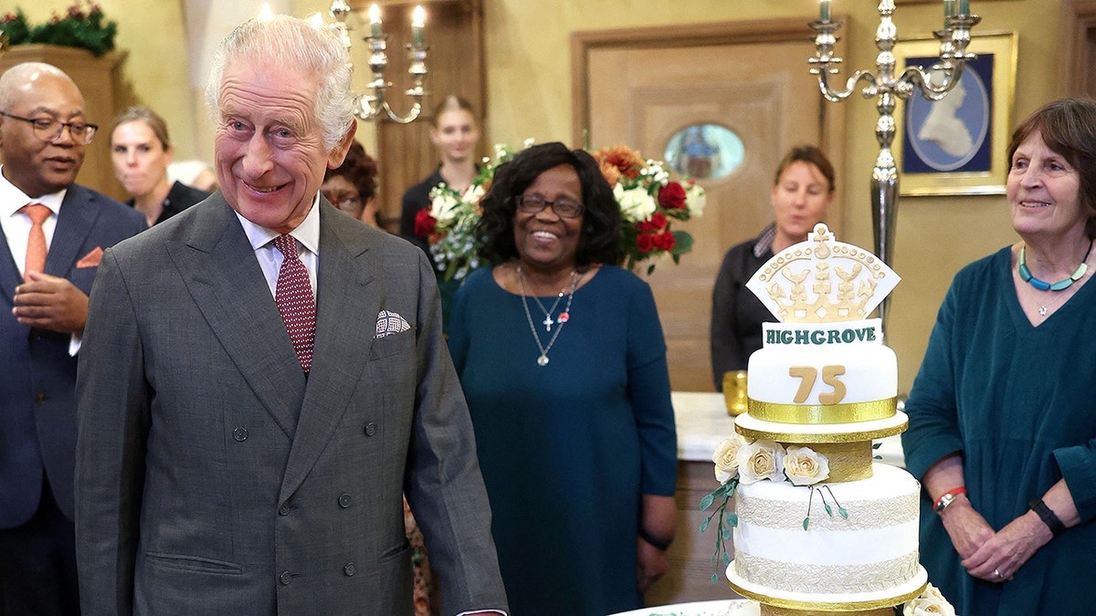 King Charles smiling next to a three-tier birthday cake
