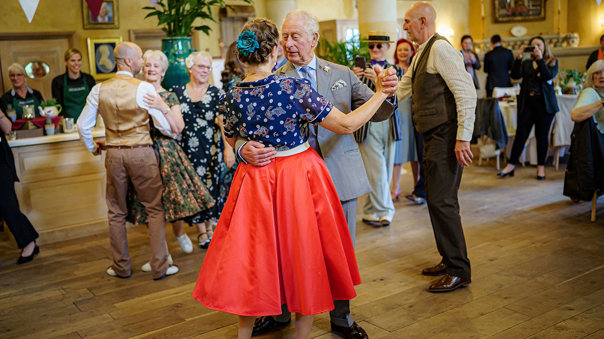 King Charles dancing with a woman wearing a blue floral blouse and red skirt