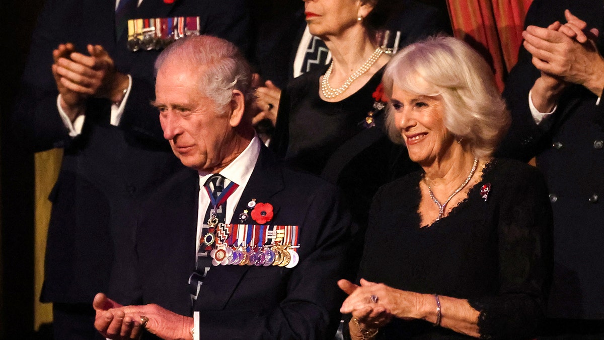 Queen Camilla smiing next to King Charles as they both wear black