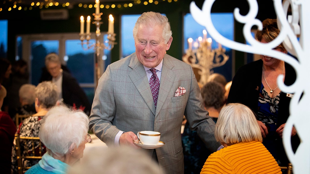 Rei Charles sorrindo para um grupo de pessoas segurando uma xícara de chá