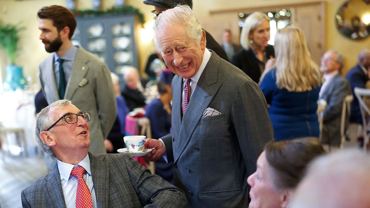 King Charles smiling to a group of people holding a cup and saucer