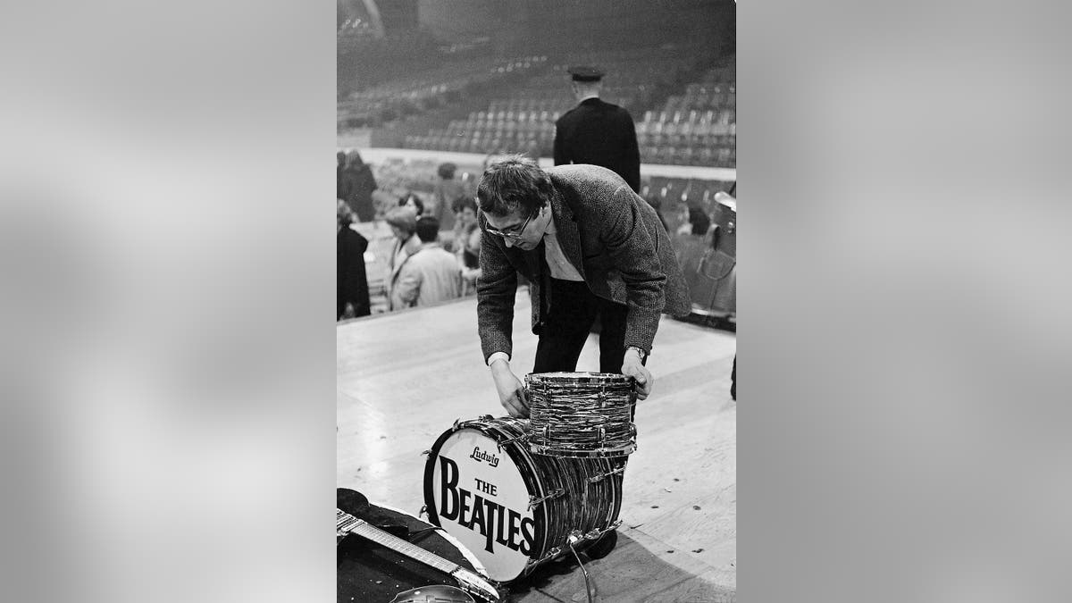 Mal Evans bending down and fixing a drum suit on a stage