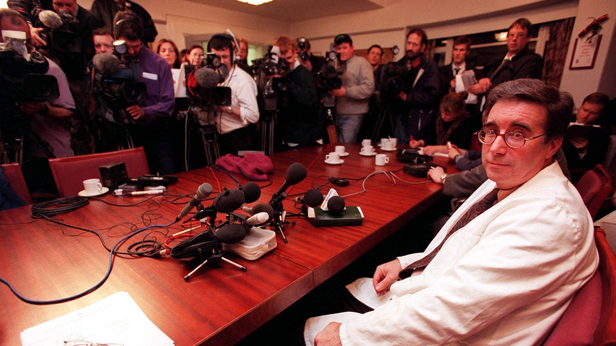 A doctor wearing a white coat looking at the camera being surrounded by photographers