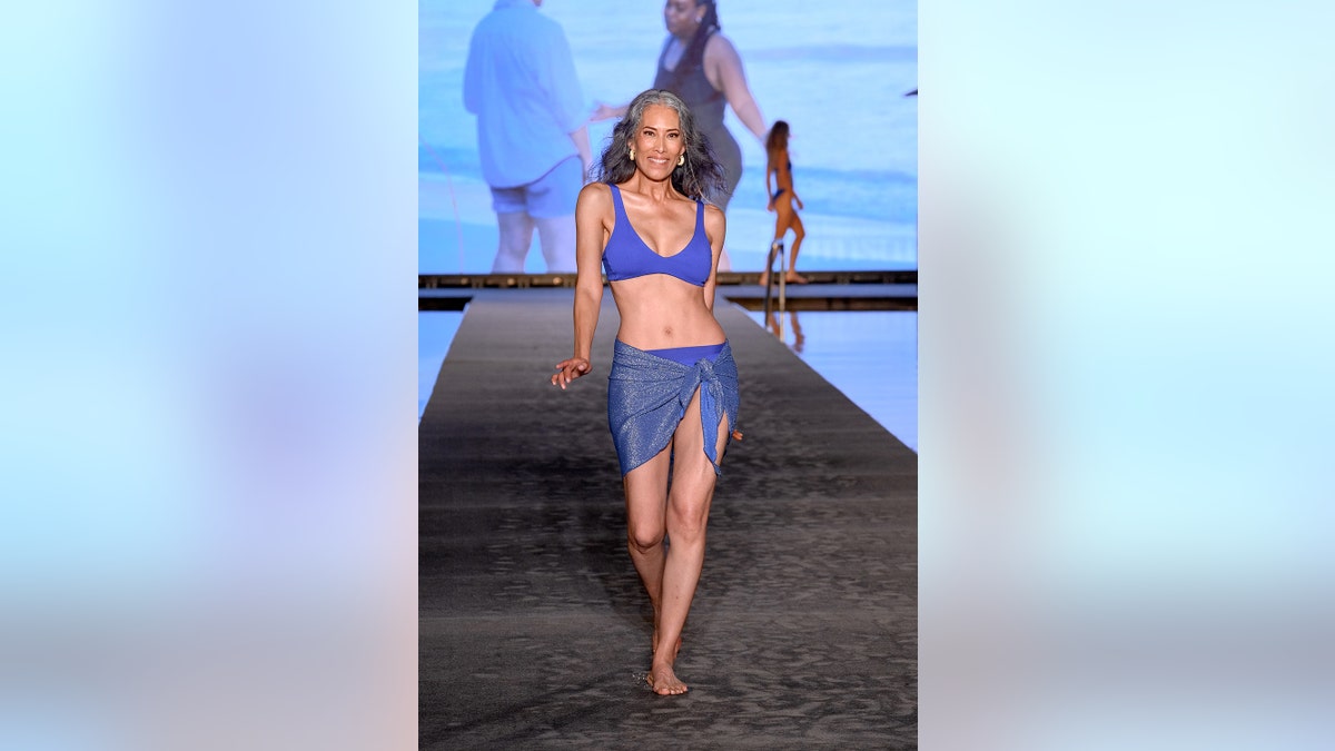Nina Cash walking the runway in a purple bikini and a matching coverup