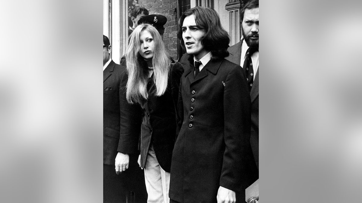 Georgr Harrison wearing a black suit next to Pattie Boyd with her hair down also wearing a black suit