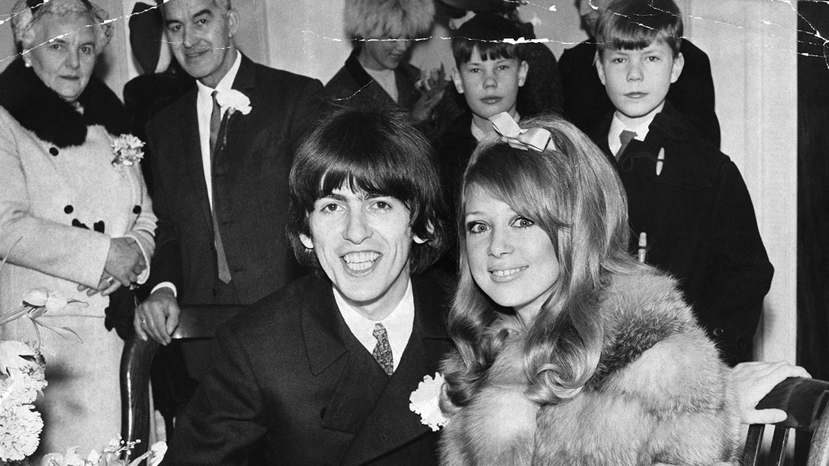 George Harrison smiling next to his bride Pattie Boyd with young people in the background